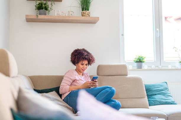 istock Mixed race woman sitting on a sofa at home and using smartphone 1321142209