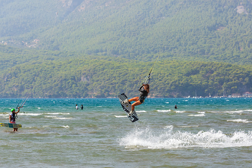 Akyaka, Mugla / Turkey - September 6 2020: Female kiteboard surfer making a jump trick in the air while another kite surfer watching her on the water in Akkaya Kiteboard Facility.