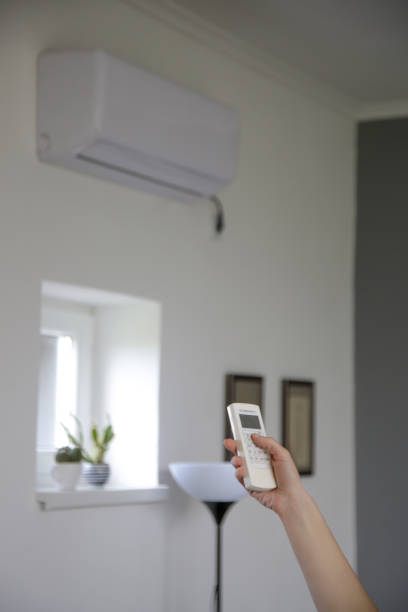 istock Human hand is using white remote of air conditioner to adjust temperature in a room. 1321144324