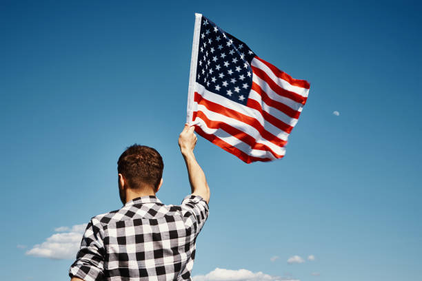 istock Man holds usa national flag against blue sky 1321146725