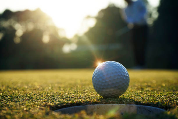 日没の背景を持つゴルフコースでのゲームで勝つためにホールゴルフの近くに緑の草を置くゴルフボール - ゴルフ ストックフォトと画像