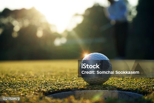 istock Golf ball putting on green grass near hole golf to win in game at golf course with sunset background 1321150973