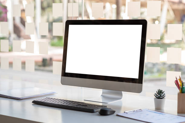 istock Computer blank white screen with a keyboard and blank papers at the window table at the office. Mock up. 1321157526