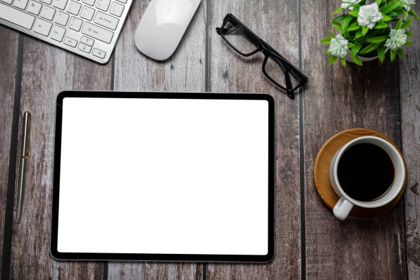 istock Tablet blank white screen with coffee notebook eyeglasses calculator on wooden desk work.````` Mock up. 1321158139