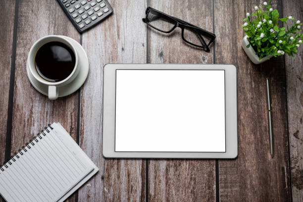 istock Tablet blank white screen with coffee notebook eyeglasses calculator on wooden desk work.````` Mock up. 1321158179