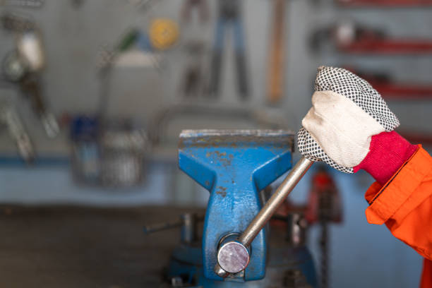 A worker who is wear cotton glove is working on the table vise grip wrench at the factory workbench in workshop area. Industrial working action photo, selective focus at human's hand.