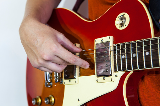 A woman's hand playing an electric guitar. Only the right hand is shown against the body of the guitar.