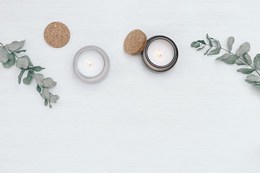 Scented burning candle in glass jar with natural ingredients on white wooden background with branches of eucalyptus and cork lid. Wellness and physical, emotional health concept. Flat lay, top view