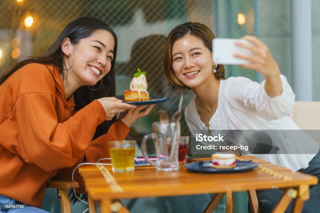 カフェで甘い食べ物を食べ、ソーシャルメディアで自分の時間を共有する女性の友人 - カフェのロイヤリティフリーストックフォト