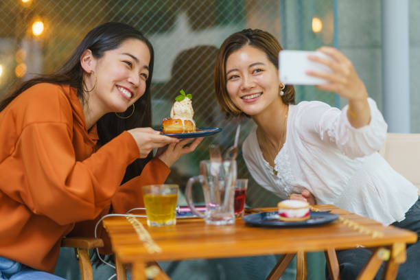 カフェで甘い食べ物を食べ、ソーシャルメディアで自分の時間を共有する女性の友人 - 楽しみ 写真 ストックフォトと画像
