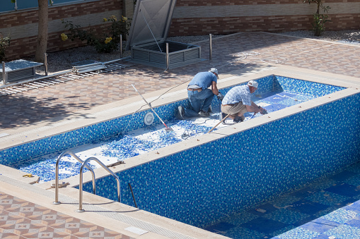Preparing for the summer season. Two workers repairing a swimming pool in the courtyard of a residential building - Mahmutlar, Alanya, Turkey - May 18, 2021