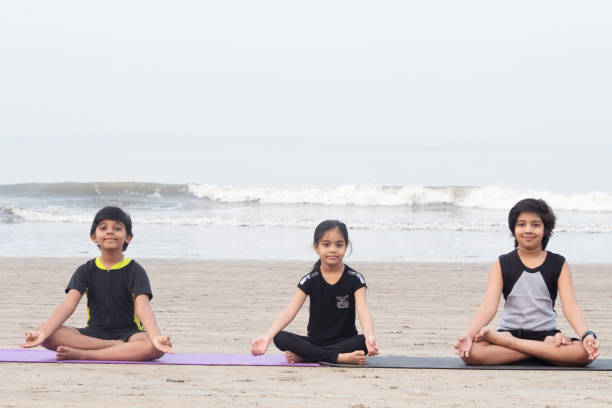 istock Cute little girl with two boys meditating on exercise mat at beach 1321169995