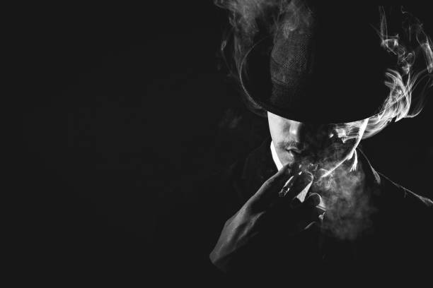 Retro man in tie and hat smoking Retro man in smoke with hat, suit and tie smoking cigarette, black and white. Noir style. mob stock pictures, royalty-free photos & images