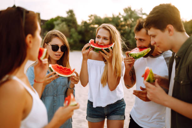 istock Young friends relaxing on the beach and eating watermelon. 1321174073