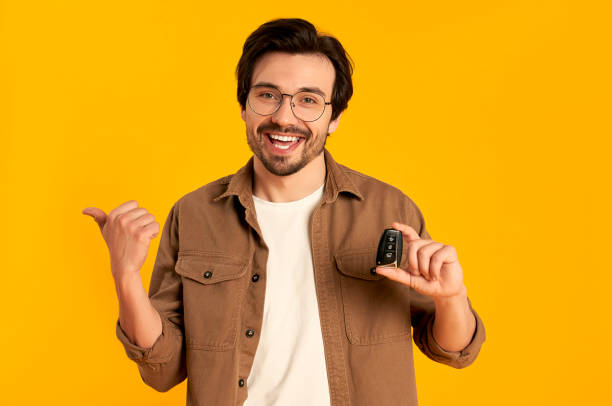 Courier Young bearded man in glasses holds keys remote control from a new car isolated on orange background. Purchase, car rental. car key stock pictures, royalty-free photos & images