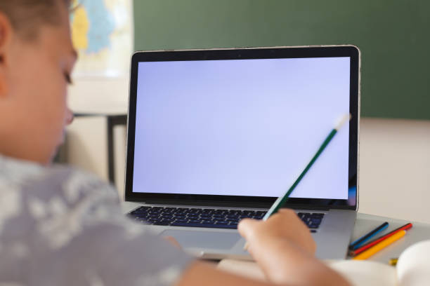 istock Caucasian boy sitting at a desk in classroom writing and using laptop, with copy space on screen 1321183063