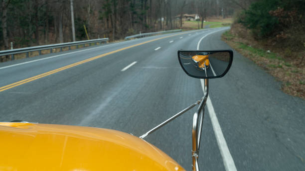 riflesso nello specchietto retrovisore dello scuolabus che guida su una strada in montagna alla fine dell'autunno - driver bus public transportation reflection foto e immagini stock