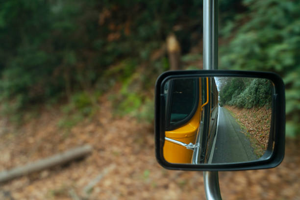 riflesso nello specchietto retrovisore dello scuolabus che guida su una strada in montagna alla fine dell'autunno - driver bus public transportation reflection foto e immagini stock