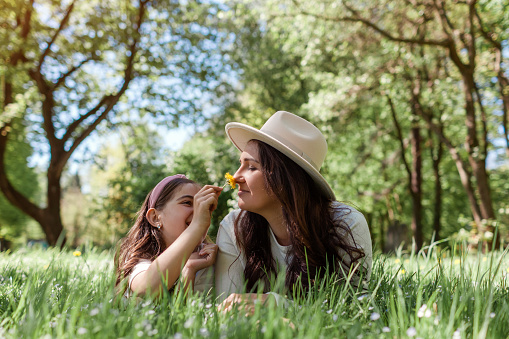 Girl gives her mother flowers to smell lying in grass in summer park. Family having fun outdoors laughing. Close up portrait