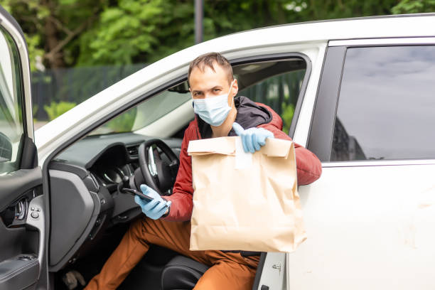 istock Postal delivery courier man wearing protective face mask in front of cargo van delivering package holding box due to Coronavirus disease or COVID-19 1321186041