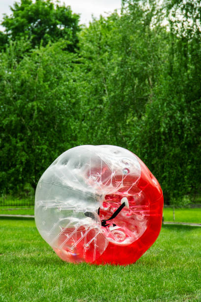 Red Zorbing Balloon on the summer lawn. Inflatable zorb ball outdoor. Leisure activity concept with vertical copy space Red Zorbing Balloon on the summer lawn. Inflatable zorb ball outdoor. Leisure activity concept with vertical copy space. zorbing stock pictures, royalty-free photos & images