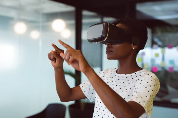 femme afro-américaine souriante utilisant un casque vr au travail - simulateur photos et images de collection