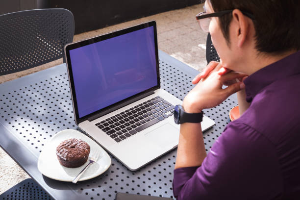 Asian businessman using laptop with blank screen sitting at table in cafe. digital nomad out and about in city concept.