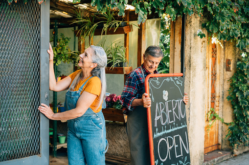 Senior couple place an open sign and open small business doors