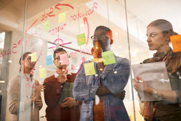 istock Pensive start-up team brainstorming in front of mind map on glass wall while working on new business project. 1321190548