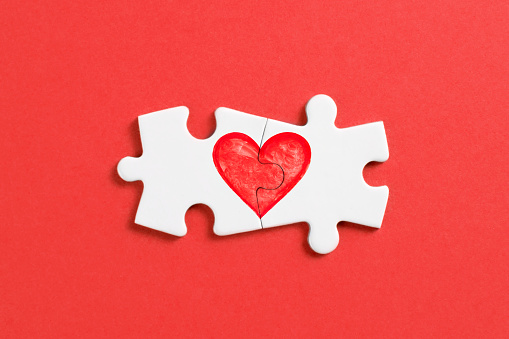 White puzzle pieces comes together to create heart shape on red background.