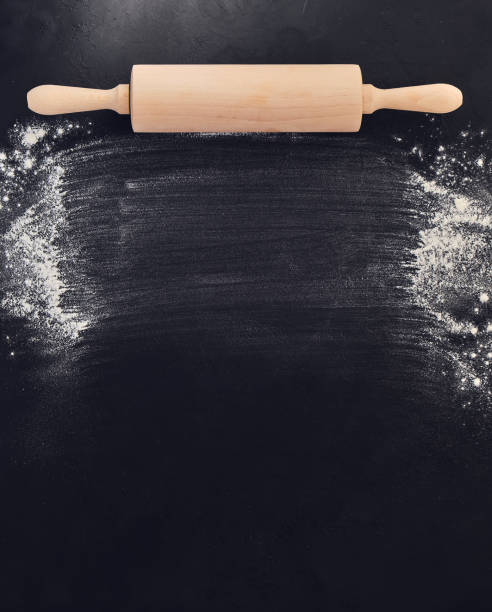 istock Wooden rolling pin in hands and flour. Bakery on a black stone background. 1321194620