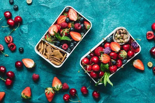 Top view of two lunch boxes with healthy food. Berries, crackers and pistachios in meal boxes over blue background.