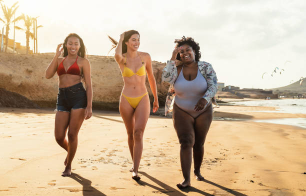 Happy multiracial females with different body size having fun walking on the beach during summer holidays Happy multiracial females with different body size having fun walking on the beach during summer holidays voluptious stock pictures, royalty-free photos & images