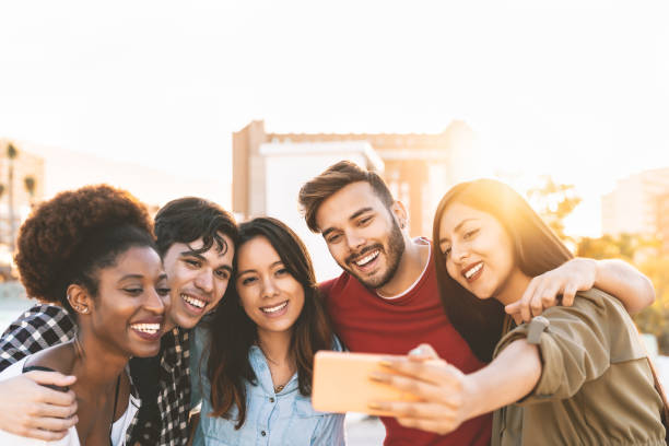 屋外のモバイルスマートフォンで自分撮りを取るグループ多民族の友人 - 屋外で楽しい幸せな混合人種の人々 - 若者ミレニアル世代と多民族ティーンエイジャーのライフスタイルコンセプト - ミレニアル世代 ストックフォトと画像