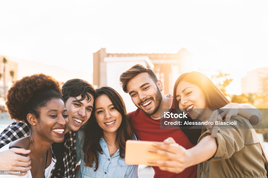 Group multiracial friends taking selfie with mobile smartphone outdoor - Happy mixed race people having fun outdoor - Youth millennial generation and multiethnic teenagers lifestyle concept Friendship Stock Photo