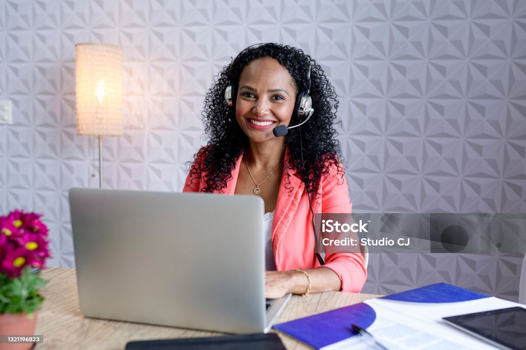 Woman looking at camera and smiling while working in contact center.. Environmental Portraits of Contact Centers and Remote Work. Connection Stock Photo