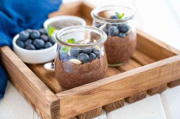 istock Chocolate chia pudding with blueberry, almonds and mint on top in a glass jar on a white wooden background. Healthy food. Copy space. 1321197043