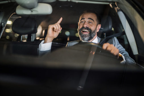Happy businessman driving his car and singing to music.