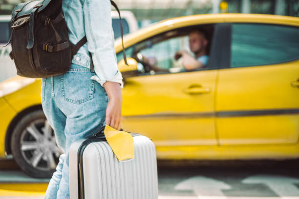 Woman waiting for taxi with face mask and travel case Young woman arrived at the airport station waiting for taxi with protective yellow face mask, backpack and travel case. Safe transportation concept yellow taxi cab stock pictures, royalty-free photos & images