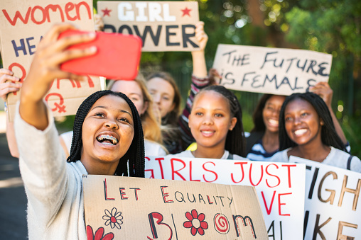 Diverse group of smiling teenage female friends with protest signs taking a selfie with a smart phone during a women's rights march