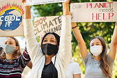 Teenage friends in face masks holding up climate change protest signs
