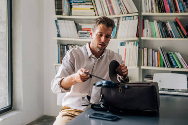 istock Handsome Young Teacher Packing his Leather Backpack in the Library 1321204793
