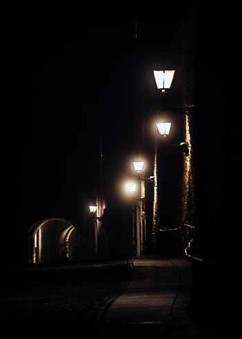 One night lamppost shines with faint mysterious yellow light through evening fog. Streetlight shine at quiet city night, magic atmospheric light in mystical darkness, copy space