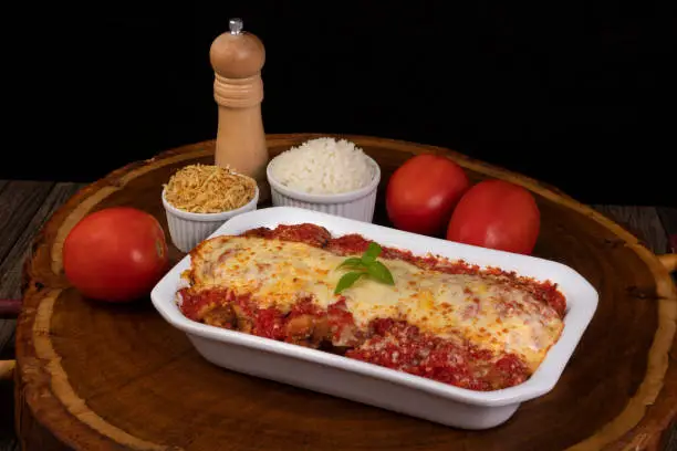 Photo of Steak Parmegiana or Parmegian Filet, made with breaded steak, tomato sauce, cheese au gratin. Accompanied by white rice and potato straw. Served in a porcelain dish. Gastronomic photo.