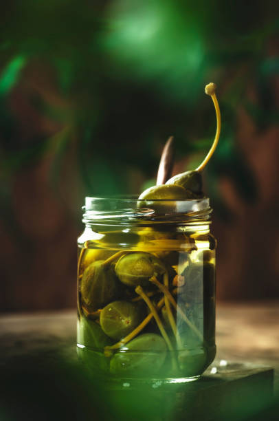 istock Capers. Marinated or pickled canned capers fruit in glass jar on wooden table, eco style still life 1321221385