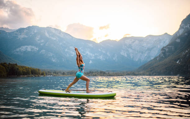 istock Mid Adult Woman Doing Warrior I Pose on Paddleboard at Dusk 1321221705