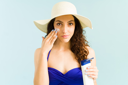 I don't want to get sunburned. Attractive caucasian woman in a swimsuit at the beach applying sunscreen lotion on her face