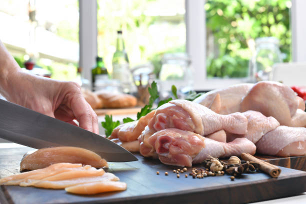 Hand slicing fresh raw chicken on a cutting board in the kitchen