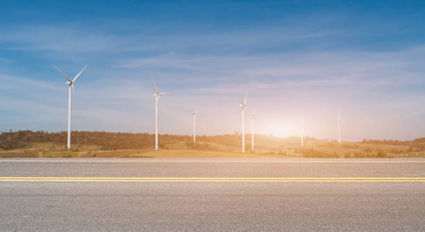 istock Asphalt road with wind turbines at sunset background 1321234353
