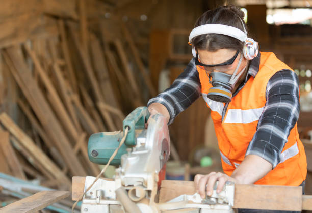 istock male carpenter wearing glasses headphone and protective mask, using electric circular saw for cutting wooden boards, on a piece of wood in workshop 1321235535